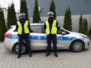 St.sierż Mateusz Kawa i sierż. Krzysztof Krawczyk na tle radiowozu. Na drugim planie zielone tuje.