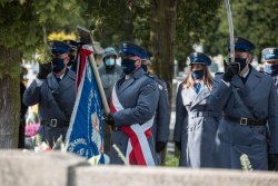 Grupa policjantów wraz z członkami kompanii honorowej na cmentarzu.