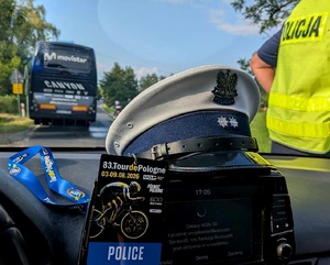 Policyjna czapka ruchu drogowego, plakietka Tour de Pologne, w tle policjant i autobus