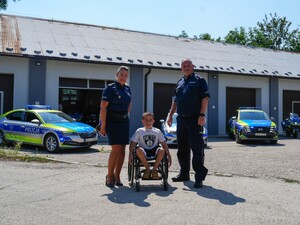 Wspólne zdjęcie z zastępca naczelnika wydziału prewencji, policjantką oraz Aleksandrem. W tle radiowozy.