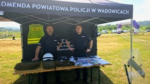 Dwóch policjantów w namiocie. Na stoliku przed nimi są ulotki oraz elementy umundurowania policyjnego