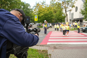 Dzieci w kamizelkach przekraczają przejście dla pieszych wraz z policjantami
