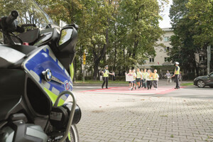 Policjanci przeprowadzający przez przejście dla pieszych dzieci ubrane w kamizelkach