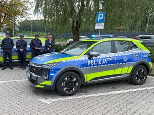 Radiowóz policyjny, w tle policjanci oraz Burmistrz Miasta i Gminy Niepołomice