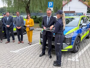 Samorządowcy z powiatu wielickiego, policjantka trzymająca kluczyki od radiowozów. W tle policjanci oraz radiowóz