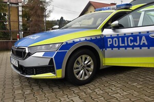 Przód oznakowanego radiowozu. Pojazd posiada otwarte i drzwi i napis Policja