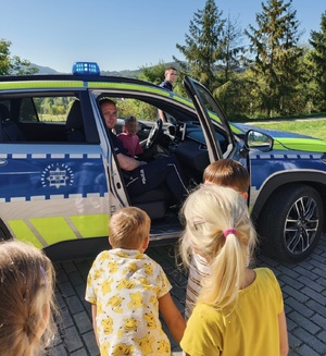 W radiowozie policjant i dziewczynka, obok samochodu dzieci i policjant