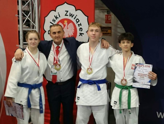Zawodnicy judo z medalami i dyplomami oraz osoba w garniturze