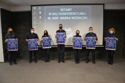 Policjanci – przedstawiciele jednostek powiatowych oraz wojewódzkiej Policji prezentujący plakat dedykowany seniorom-działkowcom.