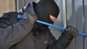 mężczyzna w kominiarce trzyma w rękach łom i próbuje nim podważyć okno