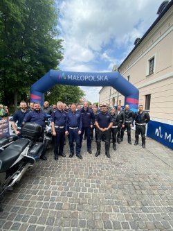 Policjanci  ruchu drogowego stojący w grupie na tle dmuchanej bramy z napisem Małopolska.