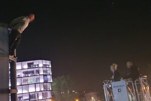 Wychylający się mężczyzna na elewacji biurowca z drugiej strony w  koszu wozu strażackiego dwóch policyjnych negocjatorów