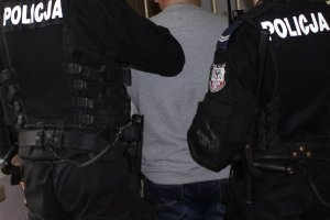 zatrzymany mężczyzna doprowadzany przez dwóch policjantów do pomieszczeń dla zatrzymanych