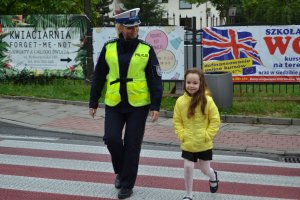 Zdjęcie przedstawia policjantkę ruchu drogowego przeprowadzającą dziewczynkę przez przejście dla pieszych.
