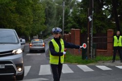 Fotografia przedstawiająca policjantkę ruchu drogowego podczas ręcznej regulacji ruchem na skrzyżowaniu. Wokół niej widać samochody będące w ruchu.