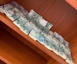 kilkadziesiąt plików banknotów o nominałach sto, pięćdziesiąt i dwadzieścia złotych oraz jeden plik w obcej walucie. Pieniądze leżą na na regale na jednej z półek