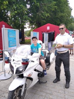 Chłopic na motorze policjanta, który stoi obok. Krynica