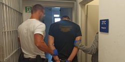 Zatrzymany mężczyzna prowadzony przez policjantów zakuty w kajdanki