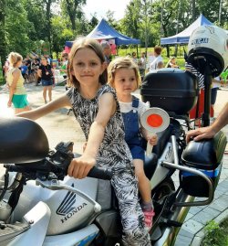 dwie dziewczynki siedzą na policyjnym motocyklu, jedna trzyma tarczę do zatrzymywania pojazdów
