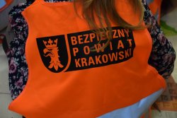 dziewczynka siedząca tyłem z założoną kamizelką odblaskowa z napisem BEZPIECZNY POWIAT KRAKOWSKI