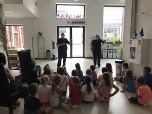 policjanci w sali edukują grupę dzieci z zakresu bezpieczeństwa w czasie wakacji