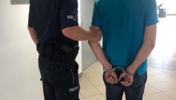 umundurowany policjant prowadzący po korytarzu komisariatu podejrzanego z założonymi na ręce trzymane z tyłu kajdankami, ustawieni tyłem