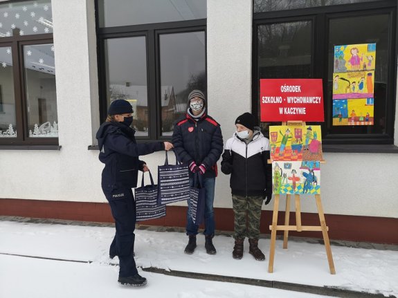 Policjant wręcza nagrody uczniom z Ośrodka Szkolno-Wychowawczego w Kaczynie, przed budynkiem placówki