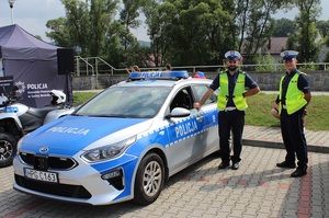 policjanci ruchu drogowego stojący w czasie pikniku przy oznakowanym radiowozie