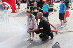 strażak wraz z dziewczynkom trzymającą wąż strażacki i lejącą wodę