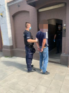 policjant trzymający za rękę zatrzymanego z kajdankami na ręce trzymane z tyłu podczas doprowadzania go do aresztu
