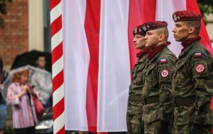Trzech żołnierzy w tle biało-czerwone flagi