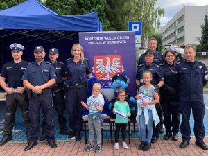 Grupa umundurowanych policjantów z kilkoma dziećmi na tle banneru Komendy Wojewódzkiej Policji w Krakowie