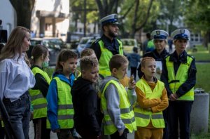 Dzieci w żółtych kamizelkach. Za nimi policjanci ruchu drogowego