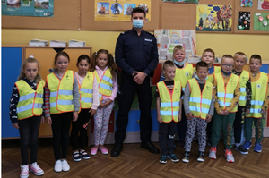 Policjant w otoczeniu dzieci ubranych w kamizelki odblaskowe