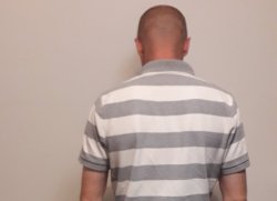 zatrzymany sprawca pobicia ubrany w białą koszulkę w szare paski stojący tyłem do zdjęcia