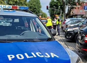 na jezdni radiowóz, w tle policjanci oraz dwóch mężczyzn przy pojeździe