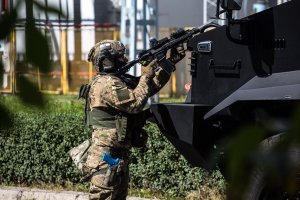 policjant mierzy z karabinka opierając się o maskę pojazdu