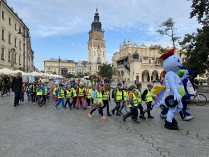 Przemarsz dzieci ubranych w kamizelki odblaskowe ulicami Krakowa w asyście policjantów