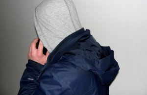 mężczyzna w bluzie z kapturem na głowie  odwrócony tyłem rozmawia przez telefon