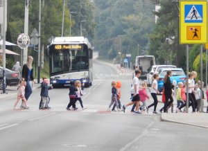 Dzieci przechodzące przez jezdnię. Na pierwszym planie znak przejścia dla pieszych.