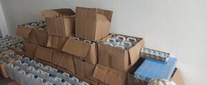 Na zdjęciu widoczne są szare kartony z zawartością białych plastikowych pojemników pięciolitrowych napełnionych spirytusem niewiadomego pochodzenia oraz paczki papierosów