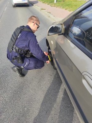 umundurowany policjant wymieniający koło w samochodzie