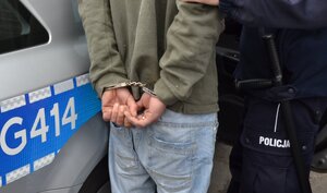 zatrzymany z kajdankami założonymi na ręce trzymane z tyłu stoi przed radiowozem