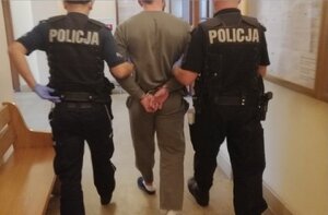Oświęcim dwaj policjanci prowadzą zatrzymanego w kajdankach założonych na ręce z tyłu, korytarzem w sądzie