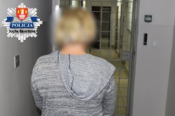 kobieta ubrana w szary swetr z kapturem stoi n tyłem do zdjęcia a przodem w kierunku wejścia do pomieszczeń dla osób zatrzymanych