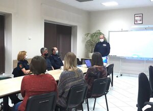 Na zdjęciu widać siedzące przy stoliku osoby, trzy kobiety siedzące tyłem oraz policjanta i dwóch funkcjonariuszy Straży Miejskiej. Obok stołu stoi policjant.