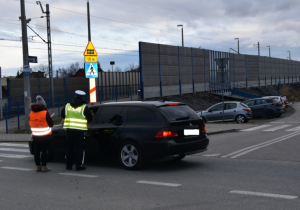 Policjant w kamizelce odblaskowej z napisem POLICJA oraz pracownik PKP Polskich Linii Kolejowych wręczają ulotki przy pojeździe osobowym (2)