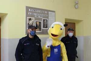 policjanci pozujący wraz z mrówka pod tablica patrona szkoły