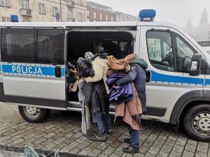 osoby bezdomne przy radiowozie trzymające ciepłą odzież otrzymaną od policjantów