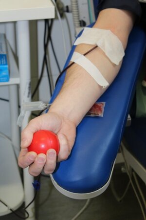 Ręka z której pobierana jest krew, w dłoni czerwona piłeczka